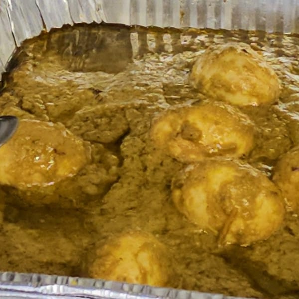 Close-up of golden-brown chicken pieces simmering in a rich, green curry sauce in a foil pan.