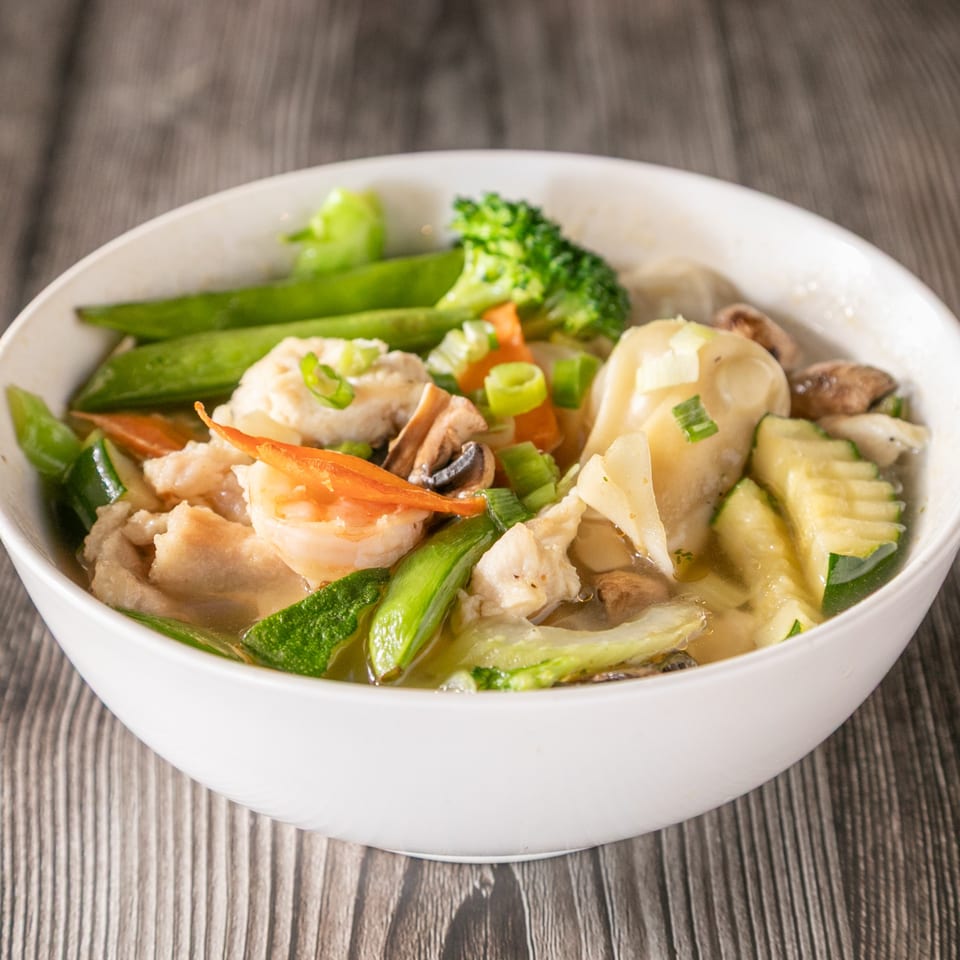 A white bowl of Vinsar's Lounge Asian-fusion soup with shrimp, chicken, dumplings, and vegetables.