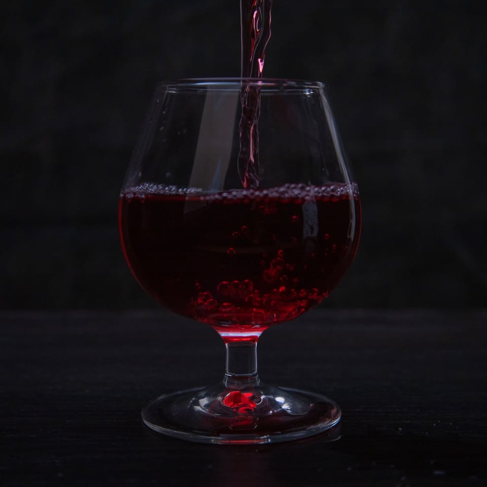 Red liquid pouring into a clear glass, creating bubbles against a dark background.
