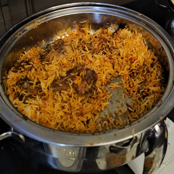 A large metal serving dish filled with chicken biryani, showing golden rice and chicken pieces.
