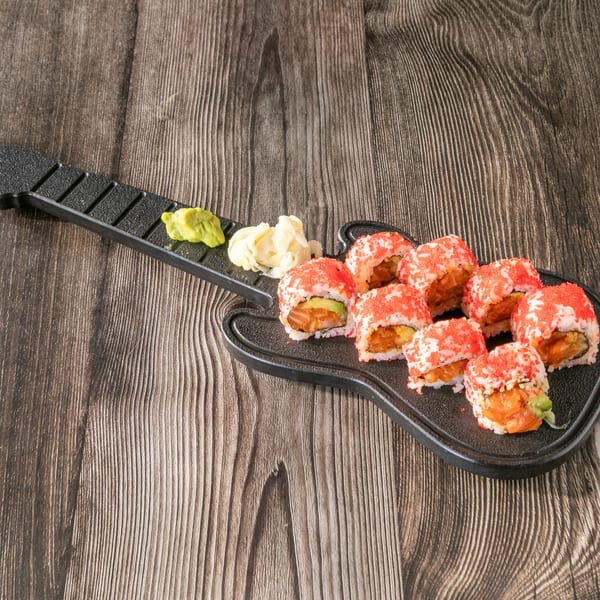 Sushi rolls with red roe, wasabi, and ginger on a guitar-shaped plate on a wooden table.