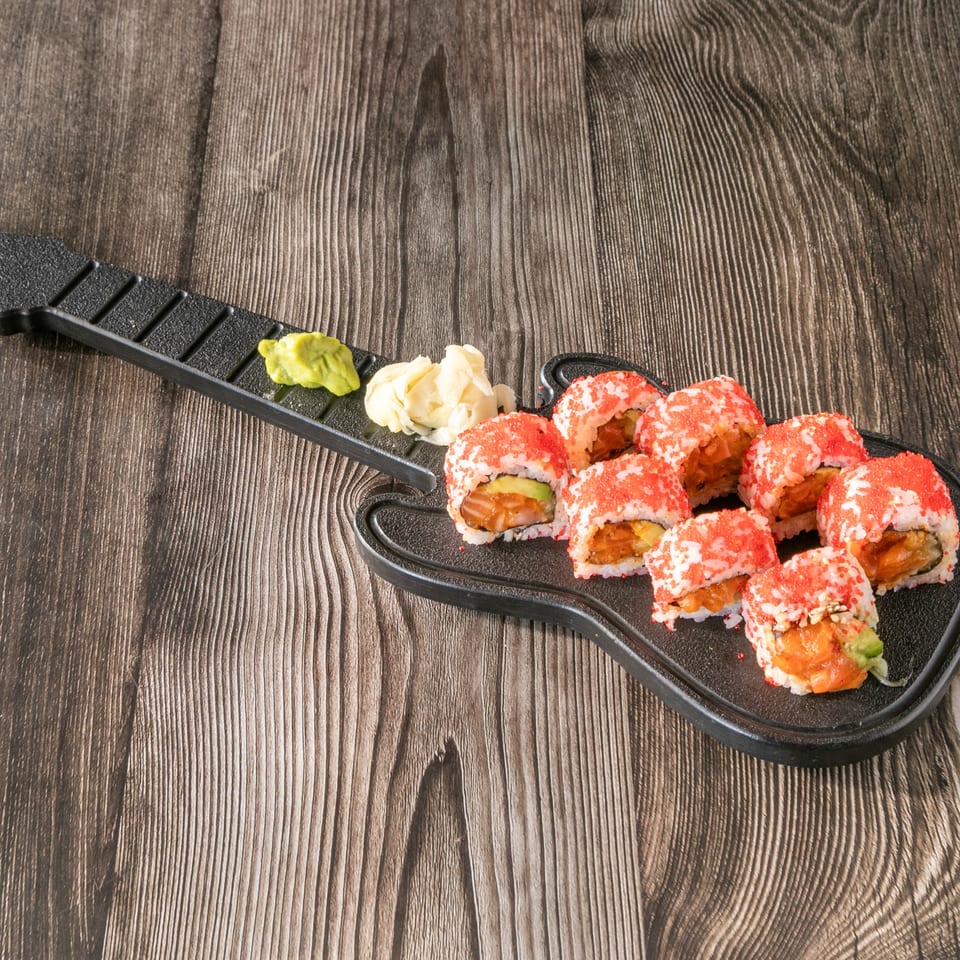 Sushi rolls with red roe, wasabi, and ginger on a guitar-shaped plate on a wooden table.