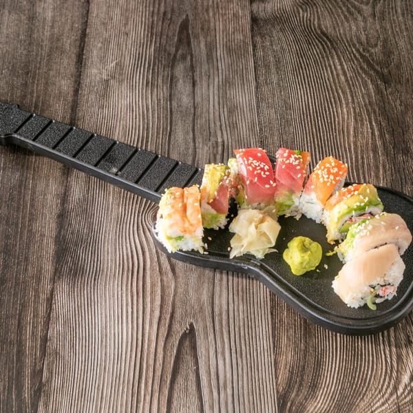 Assorted sushi rolls, including tuna, salmon, and shrimp, arranged on a guitar-shaped platter with wasabi and ginger.