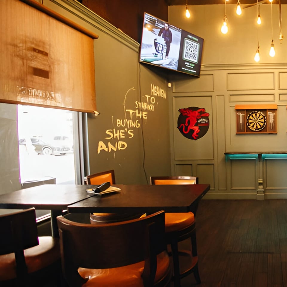 Interior of Vinsar's Lounge with tables, chairs, a TV, dartboard, and street view.