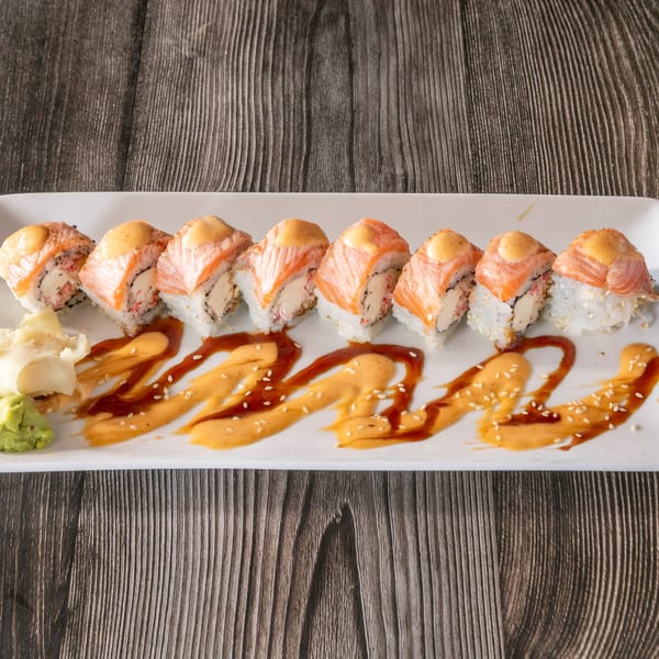 A plate of Vinsar's Lounge sushi rolls with salmon, sauce, wasabi, and ginger on a wooden table.