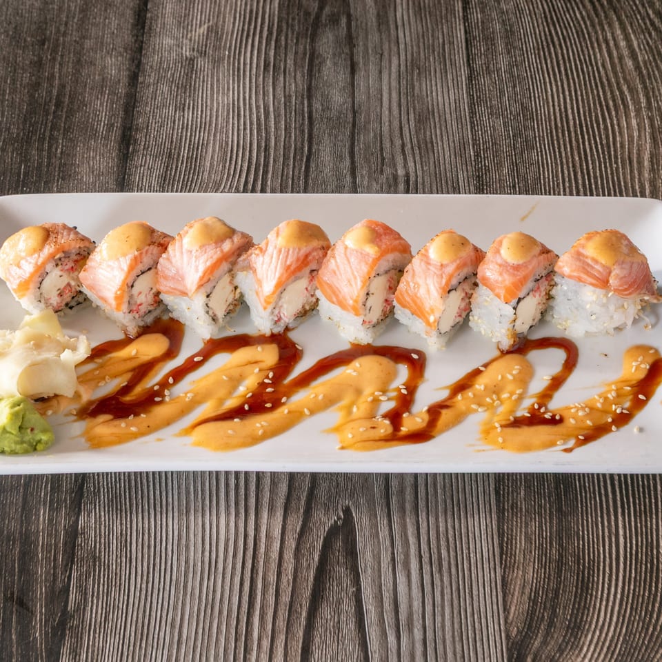 A plate of Vinsar's Lounge sushi rolls with salmon, sauce, wasabi, and ginger on a wooden table.